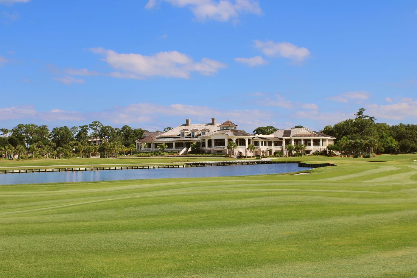 Grand Low-Country golf clubhouse across the fairway and lake, framed by palms
