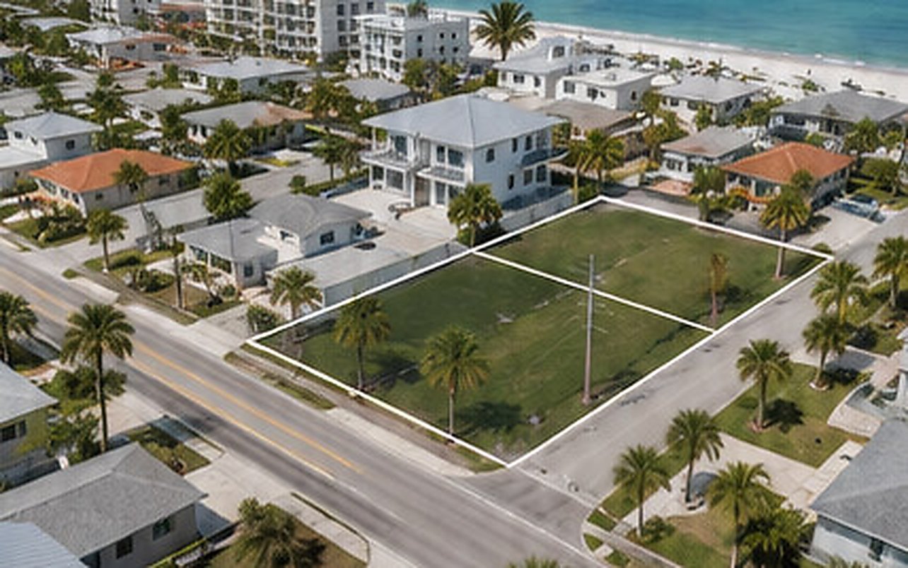Aerial view of a vacant grass corner lot outlined in white, surrounded by streets and single-storey houses in a coastal block