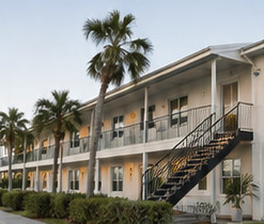 Two-storey residential building with an exterior stair and balcony walkway, framed by palm trees